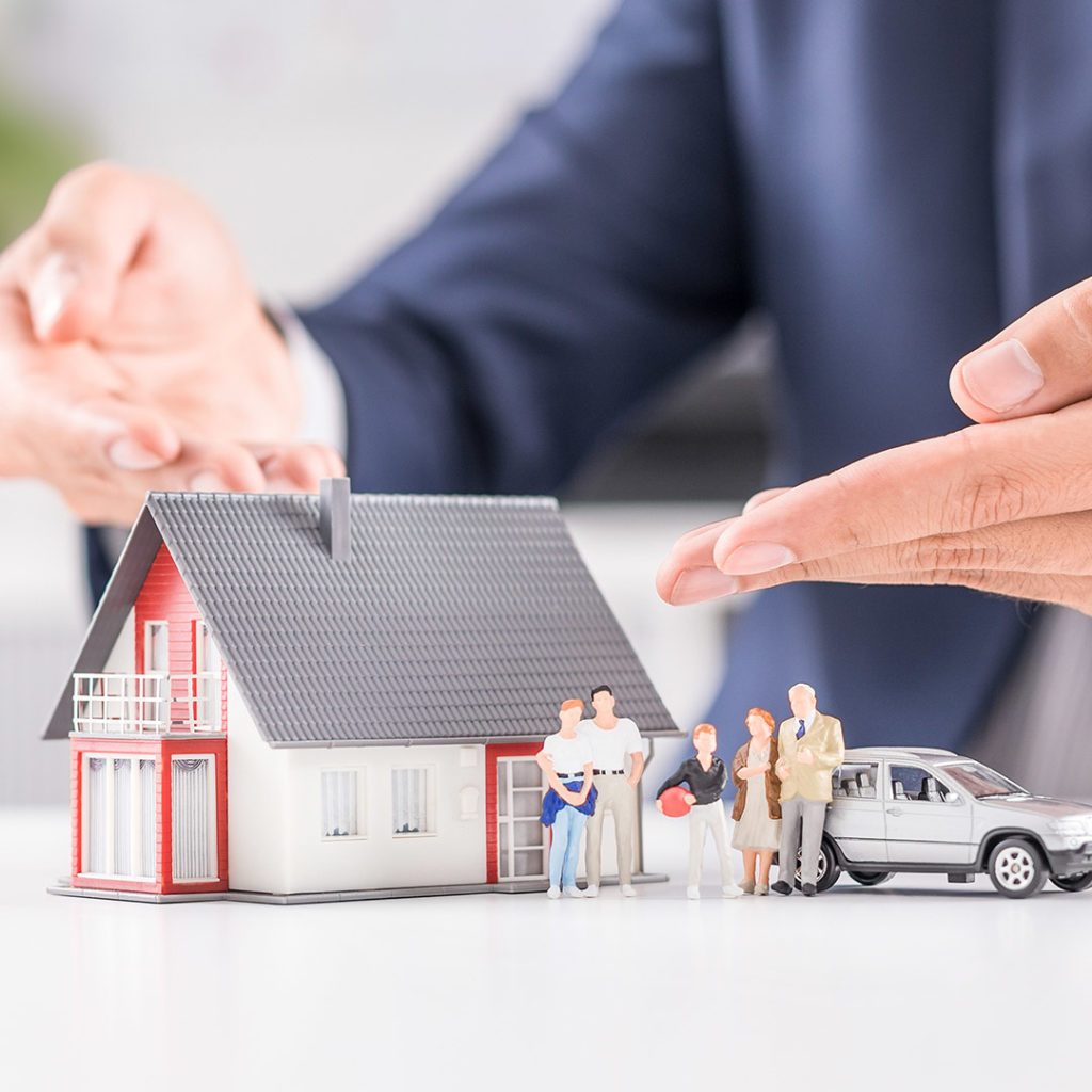 insurance-agent-pointing-at-a-house-toy-that-is-next-to-a-family-and-car-toy-casper-wy